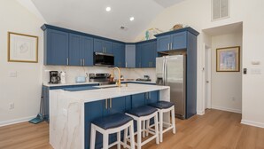 A modern kitchen with blue cabinets, a white marble island, and stainless steel appliances. - Walk to Beach, Heated Pool, Hot Tub, Dogs OK! (Kitty Hawk)