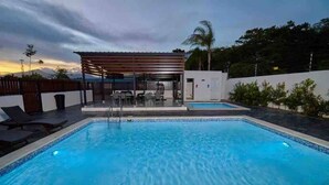 Una piscina con zona de estar techada y sillones de descanso.