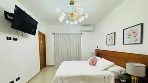 Un dormitorio con cama, televisor montado en la pared, candelabro y cuadros enmarcados.