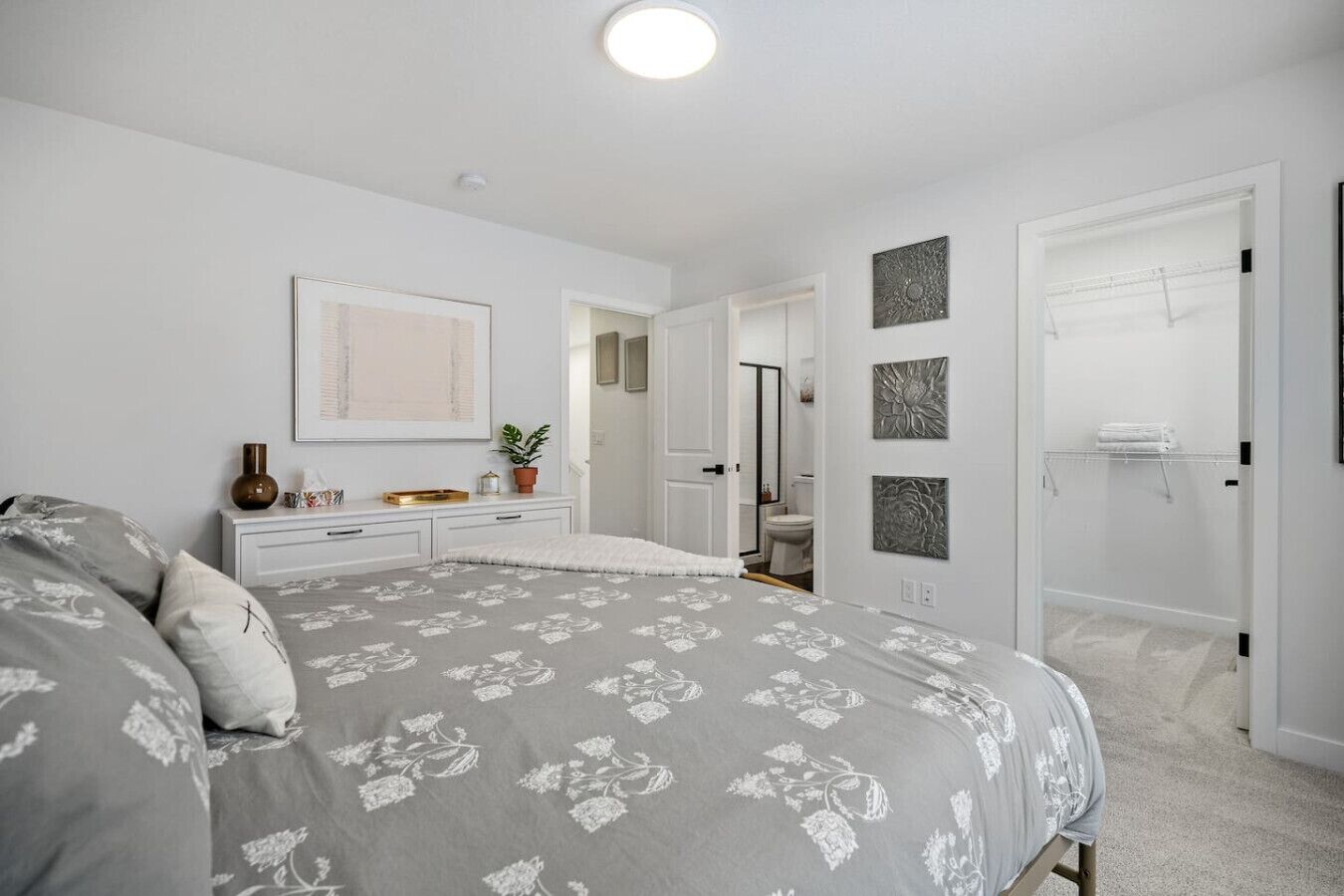 A bedroom with a bed, bedside table, dresser, and a bathroom visible through an open door.