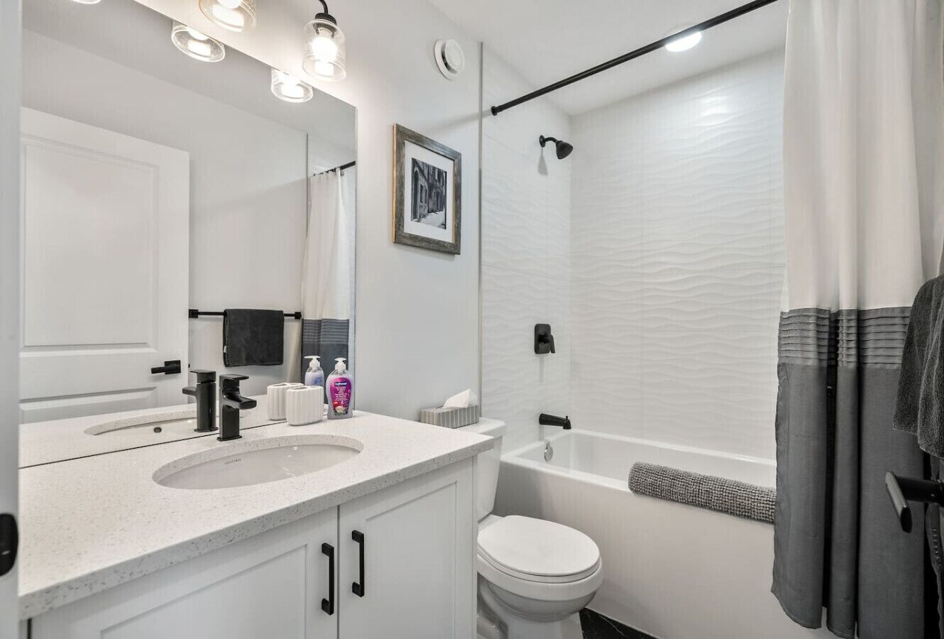 Un bagno moderno con lavandino, water e vasca da bagno bianchi. Un quadro appeso alla parete e un porta asciugamani con un asciugamano.