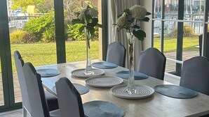 A dining area with a table set for four, surrounded by chairs, with a view of a garden and buildings outside.