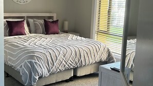 A bedroom with a bed, a decorative wall piece, a window with blinds, and a mirror.