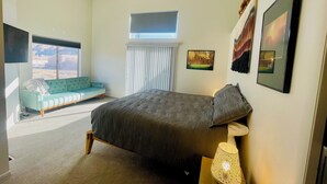 Un dormitorio con cama, sofá azul, ventilador de techo y ventana con persianas.