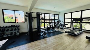 Un gimnasio con diverso equipo de ejercicio, amplias ventanas y suelo de madera.