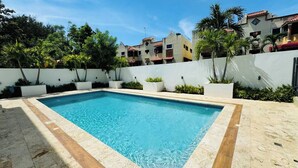 Una piscina rectangular con agua azul cristalina, rodeada por un solado de azulejos y macetas blancas con follaje.