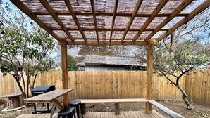 Een houten terras met een pergola, een barbecue en een picknicktafel.