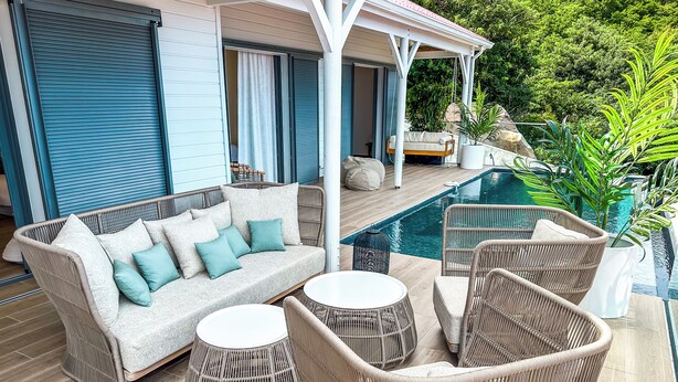 Un área junto a la piscina con muebles de mimbre, un sofá y una mesita.