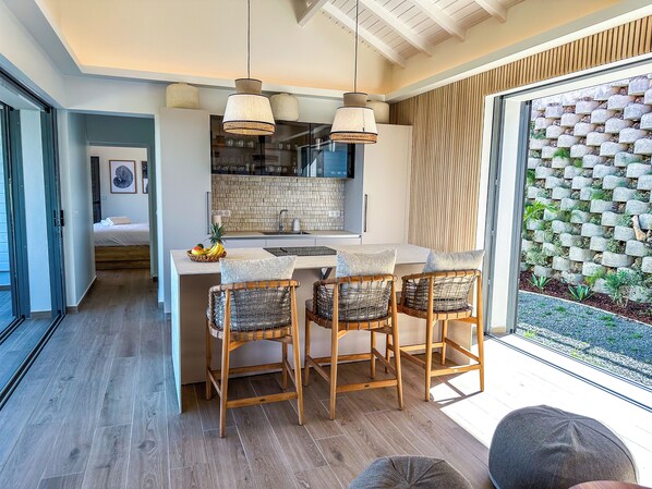 Une cuisine moderne dotée d’un îlot central, de chaises en bois et de luminaires suspendus.