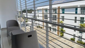 A balcony with two wicker chairs, a metal railing, and a view of a white building with multiple windows and balconies.