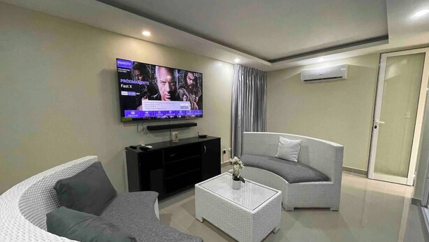 A modern living room with a flat-screen TV, two white wicker sofas, a coffee table, and a sliding glass door.