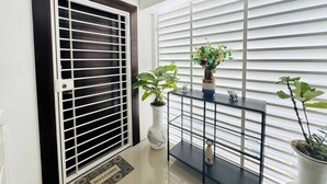 A modern entryway with a dark-framed door labeled 'C4', a welcome mat, a console table with decorative items, and a large window with horizontal blinds.