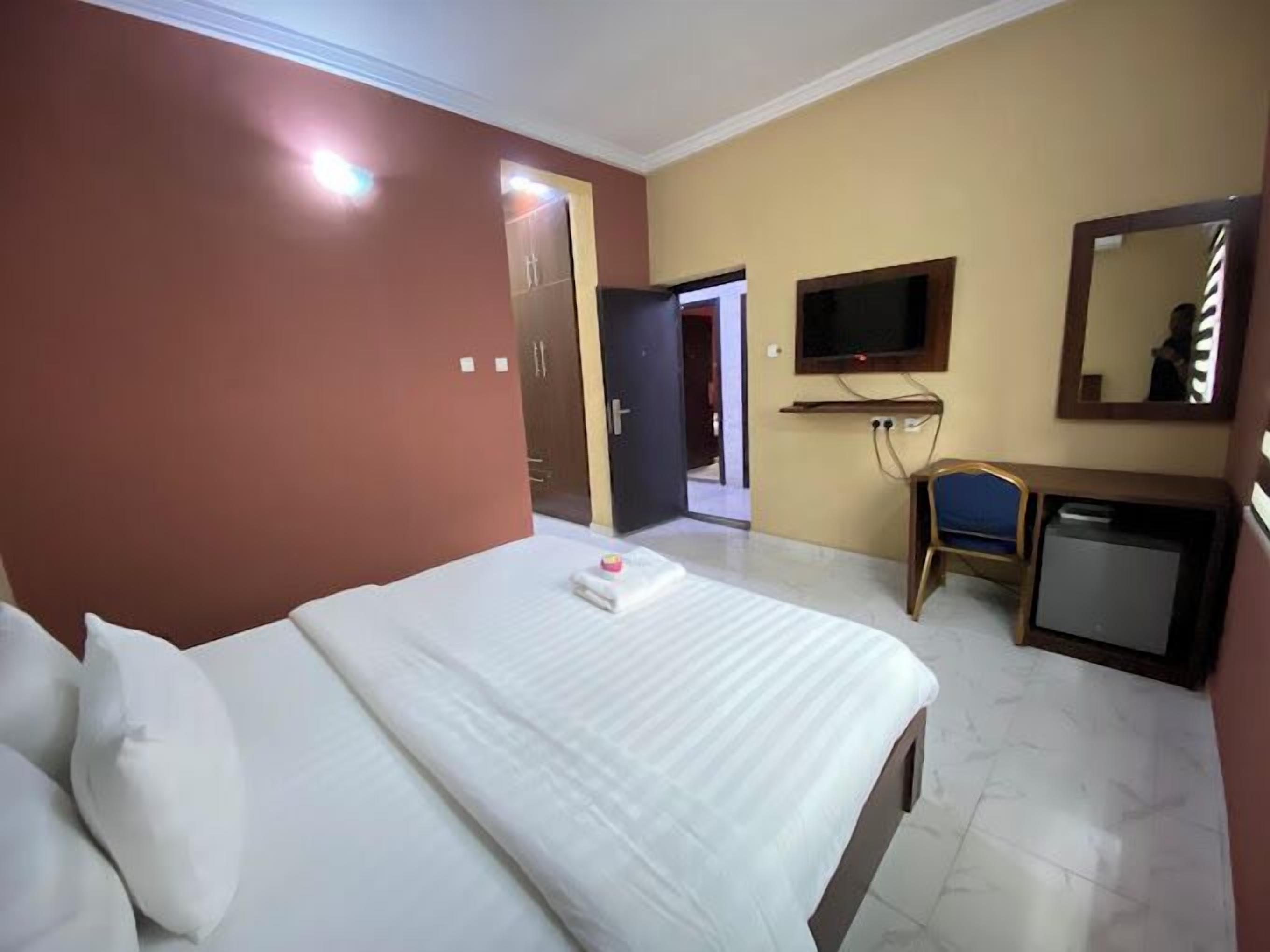 A hotel room with a bed, a desk, a chair, a television, and a mirror.