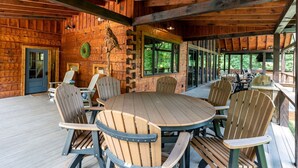 A wooden cabin with a round table and chairs, a door, and a window overlooking greenery. - Nite Owl-Luxury Log Cabin Rental, Outdoor Fire Pit, Fire Place, High Speed Internet, Hot Tub, Pool Table, Open Concept- Nantahala NC (Topton)