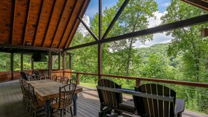 An outdoor wooden deck with a table and chairs, surrounded by a forested landscape. - Nite Owl-Luxury Log Cabin Rental, Outdoor Fire Pit, Fire Place, High Speed Internet, Hot Tub, Pool Table, Open Concept- Nantahala NC (Topton)
