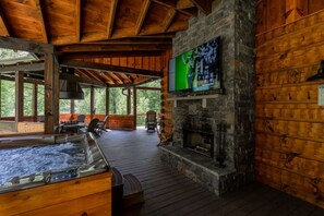 A wooden cabin interior with a stone fireplace, a hot tub, and a television mounted on the wall. - Nite Owl-Luxury Log Cabin Rental, Outdoor Fire Pit, Fire Place, High Speed Internet, Hot Tub, Pool Table, Open Concept- Nantahala NC (Topton)