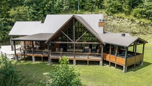 A cabin with a large deck, multiple seating areas, and a prominent chimney. - Nite Owl-Luxury Log Cabin Rental, Outdoor Fire Pit, Fire Place, High Speed Internet, Hot Tub, Pool Table, Open Concept- Nantahala NC (Topton)