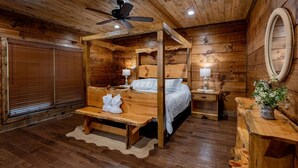 A wooden cabin-style bedroom with a four-poster bed, two bedside tables with lamps, a bench with towels, and a wooden headboard. - Nite Owl-Luxury Log Cabin Rental, Outdoor Fire Pit, Fire Place, High Speed Internet, Hot Tub, Pool Table, Open Concept- Nantahala NC (Topton)