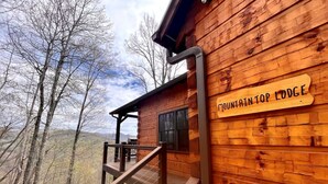 A wooden lodge with a sign reading 'Mountain Top Lodge,' a staircase, and a view of trees and mountains.