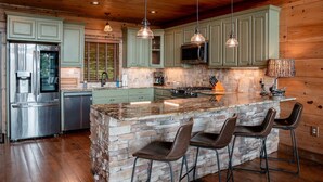 A kitchen with a large island, bar stools, a refrigerator, and a microwave.