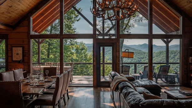 A spacious room with a large dining table, leather seating, and a view of a mountainous landscape through expansive windows.