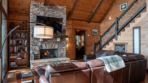 A cozy living room with a stone fireplace, leather sofa, and a staircase.