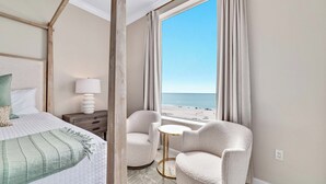 Habitación de hotel con cama, una silla, una mesita y vista a la playa.
