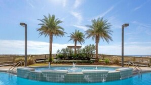 Una piscina con una fuente, rodeada de palmeras y una terraza de madera.