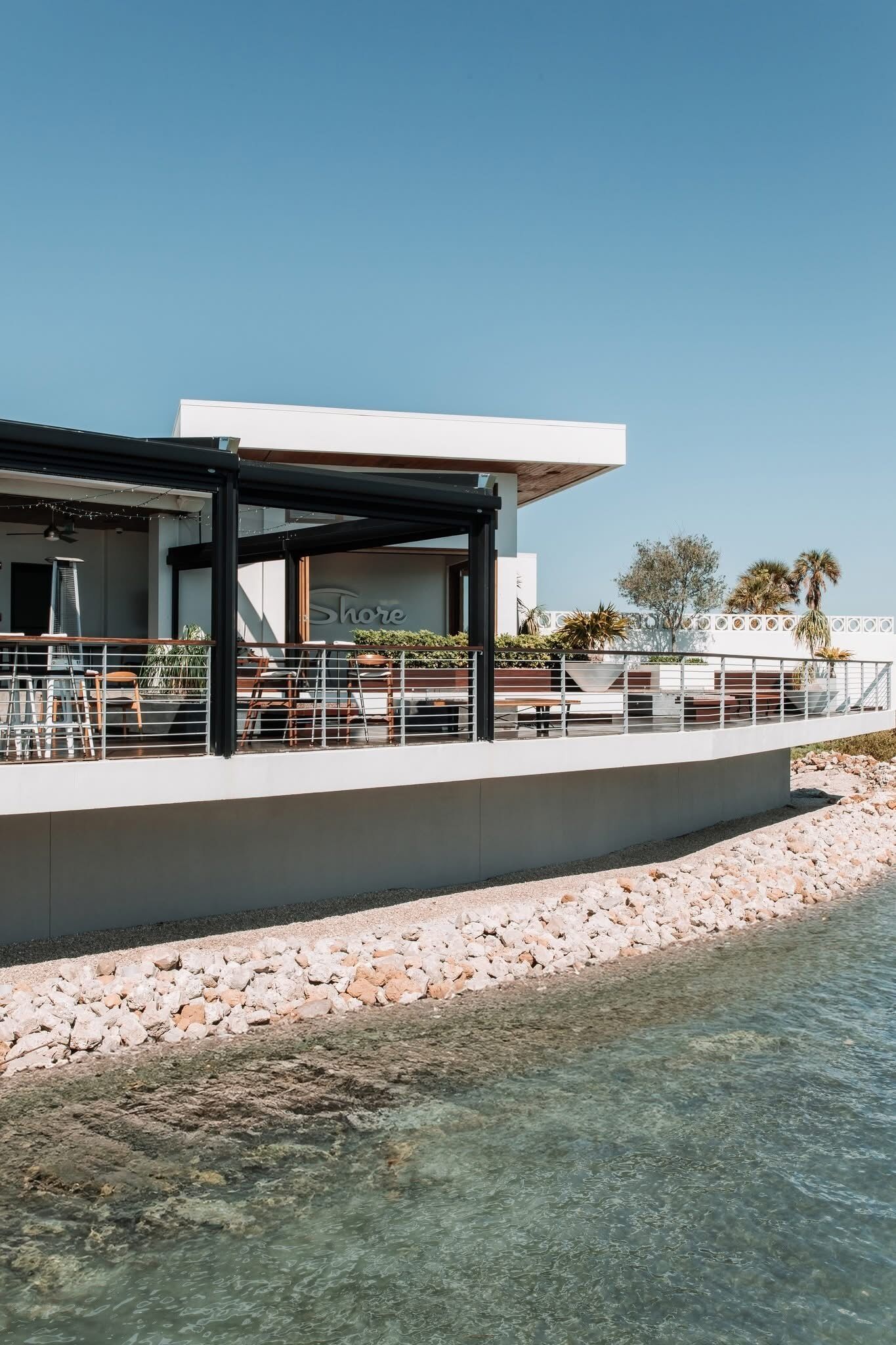 Restaurante à beira-mar com mesas ao ar livre, um alpendre coberto e vista clara para a água.