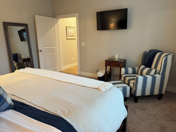 A bedroom with a large bed, a chair, a TV, and a door.
