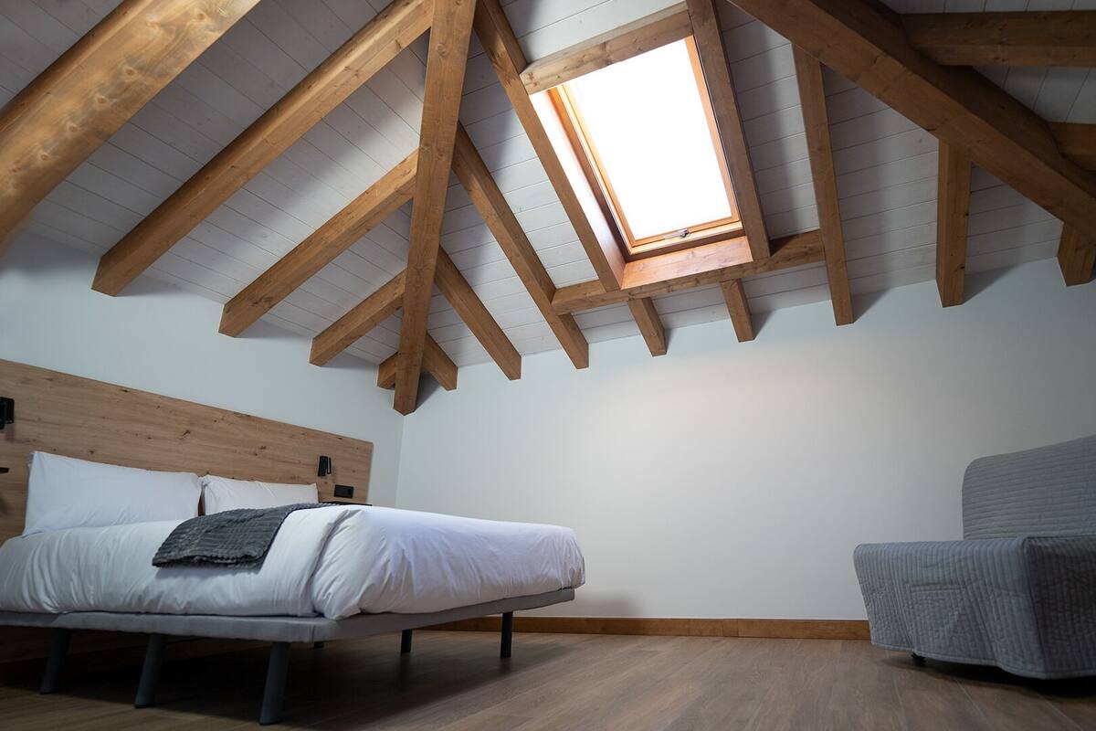 Un dormitorio con techo inclinado, una cama, una silla y un tragaluz.
