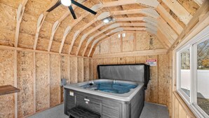 Een hottub in een houten constructie, met een plafondventilator, een raam en een waarschuwingsbord.