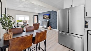 Een moderne keuken met roestvrijstalen apparatuur, een eetgedeelte met lederen stoelen en een woonkamer met televisie en behang met een patroon.