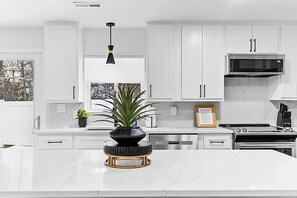 A modern kitchen with white cabinetry, a central island, a black pendant light, and a stainless steel microwave. - The Getaway House | St Charles 4BR Sleeps 11 Game Room | Hot Tub | Mercer Stays (Saint Charles)