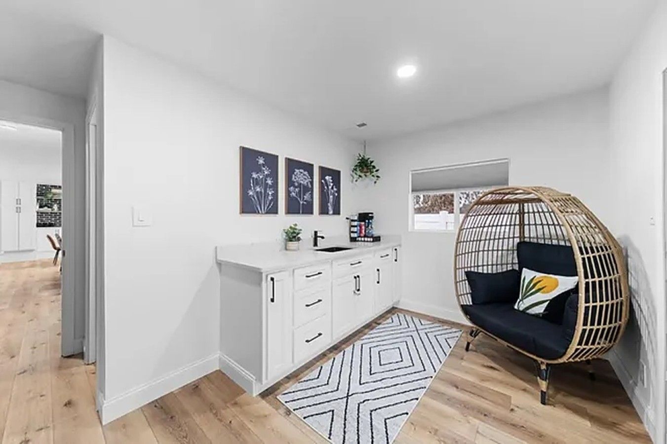 A modern kitchen with white cabinets, a hanging chair, and a geometric rug.