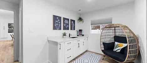 A modern kitchen with white cabinets, a hanging chair, and a geometric rug.