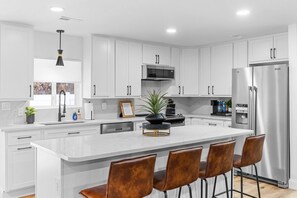 A modern kitchen with white cabinetry, a central island with chairs, stainless steel appliances, and a pendant light. - The Getaway House | St Charles 4BR Sleeps 11 Game Room | Hot Tub | Mercer Stays (Saint Charles)