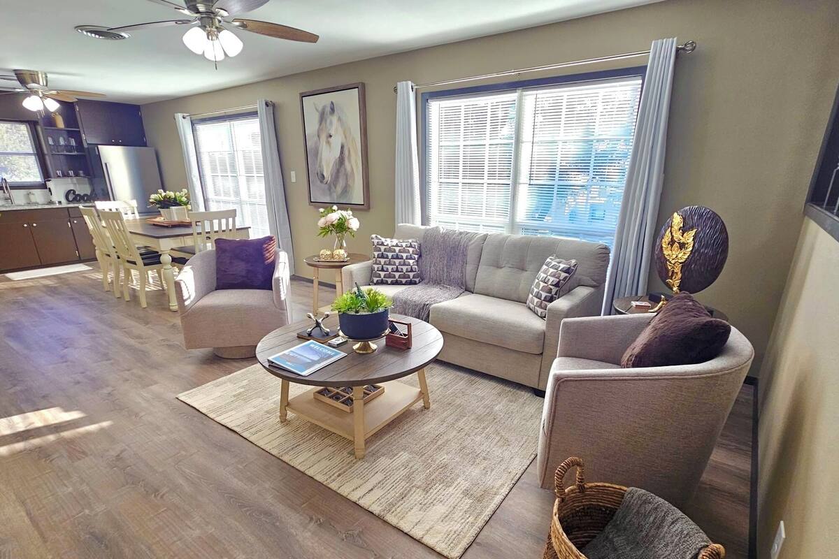 Una sala moderna con un sofá, sillones, una mesa de centro y un comedor con sillas y una mesa.