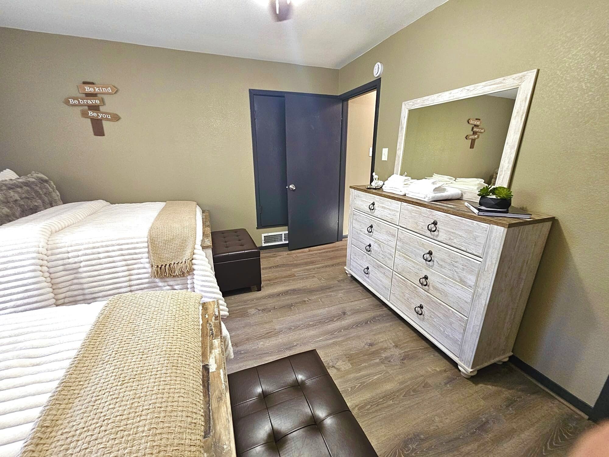 A bedroom with a bed, a dresser, a mirror, and a wall with motivational signs.