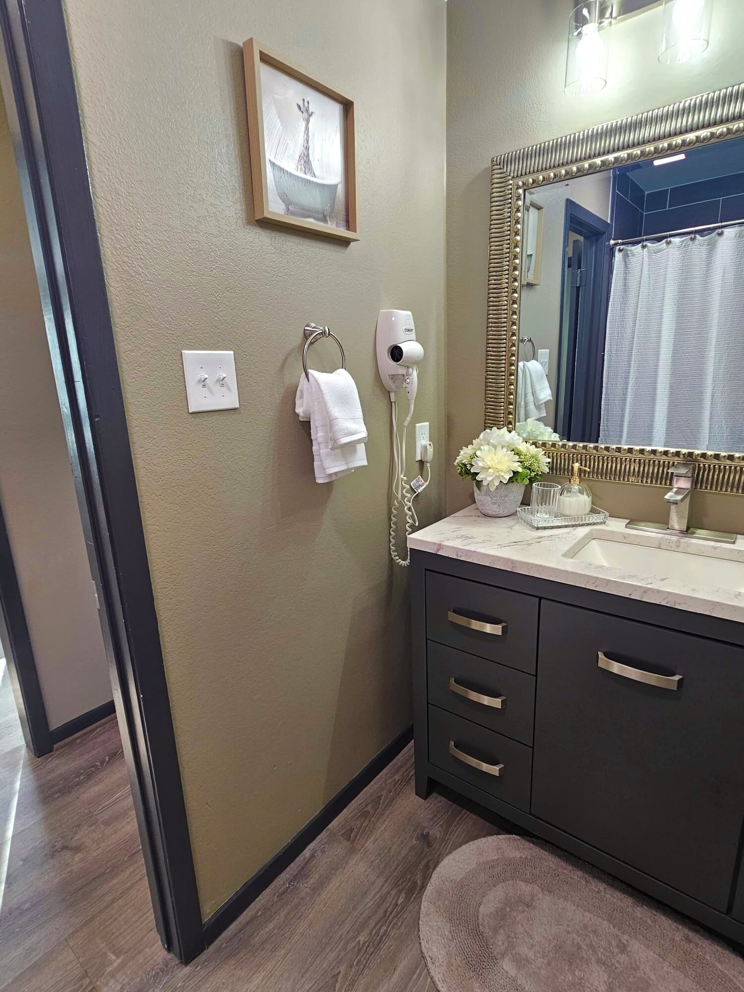 A bathroom with a vanity, a large mirror, a hairdryer, and a framed picture on the wall.