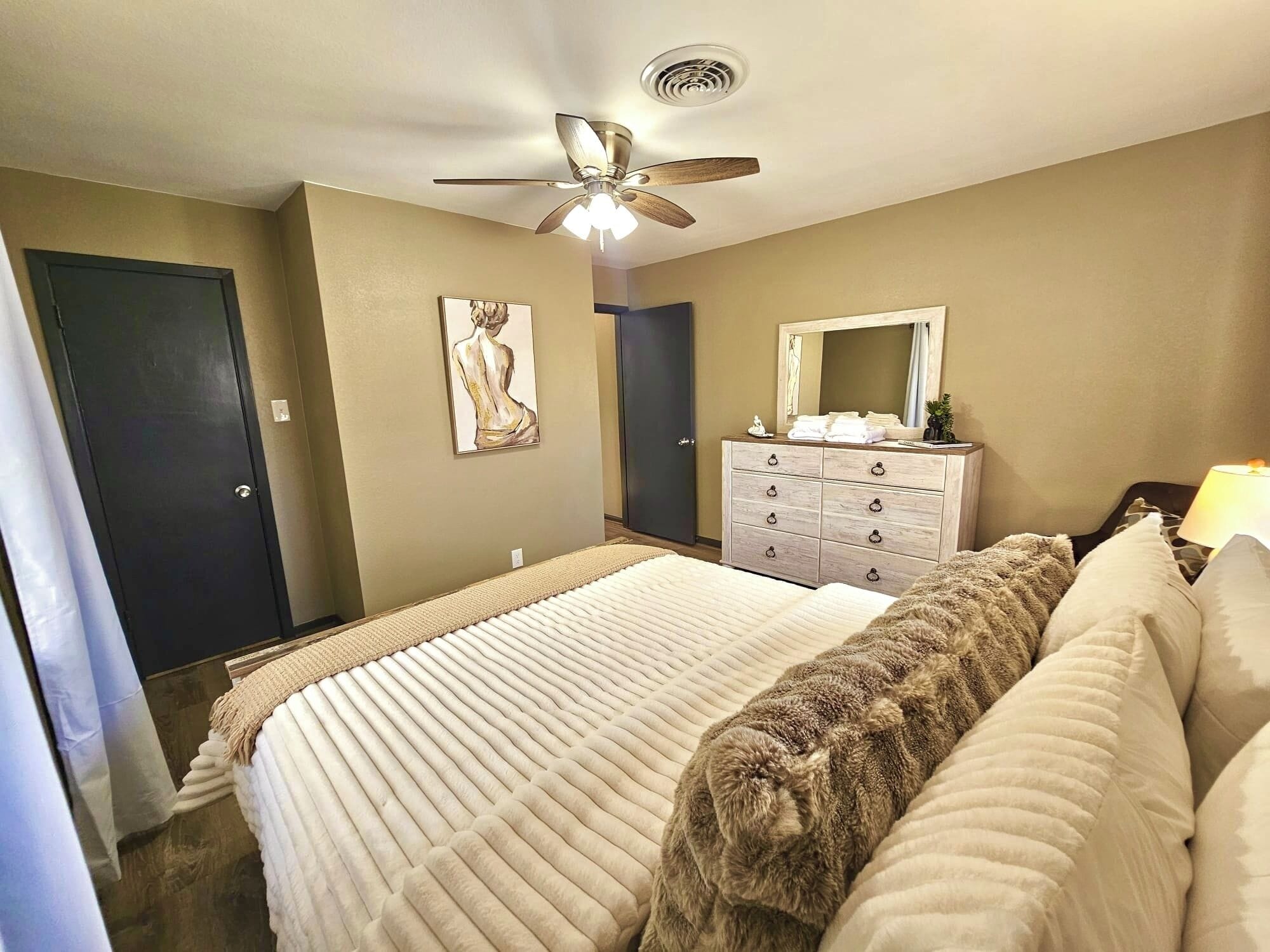 Ein Schlafzimmer mit Bett, Deckenventilator, Kommode und Spiegel.