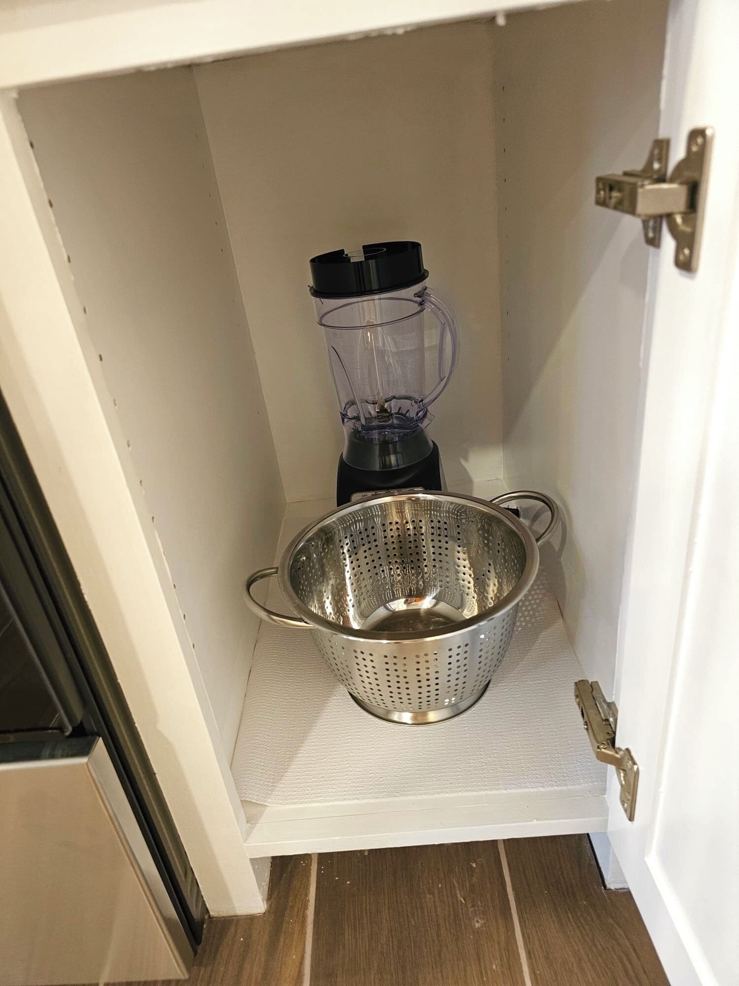 A kitchen with a blender and a colander on the countertop.