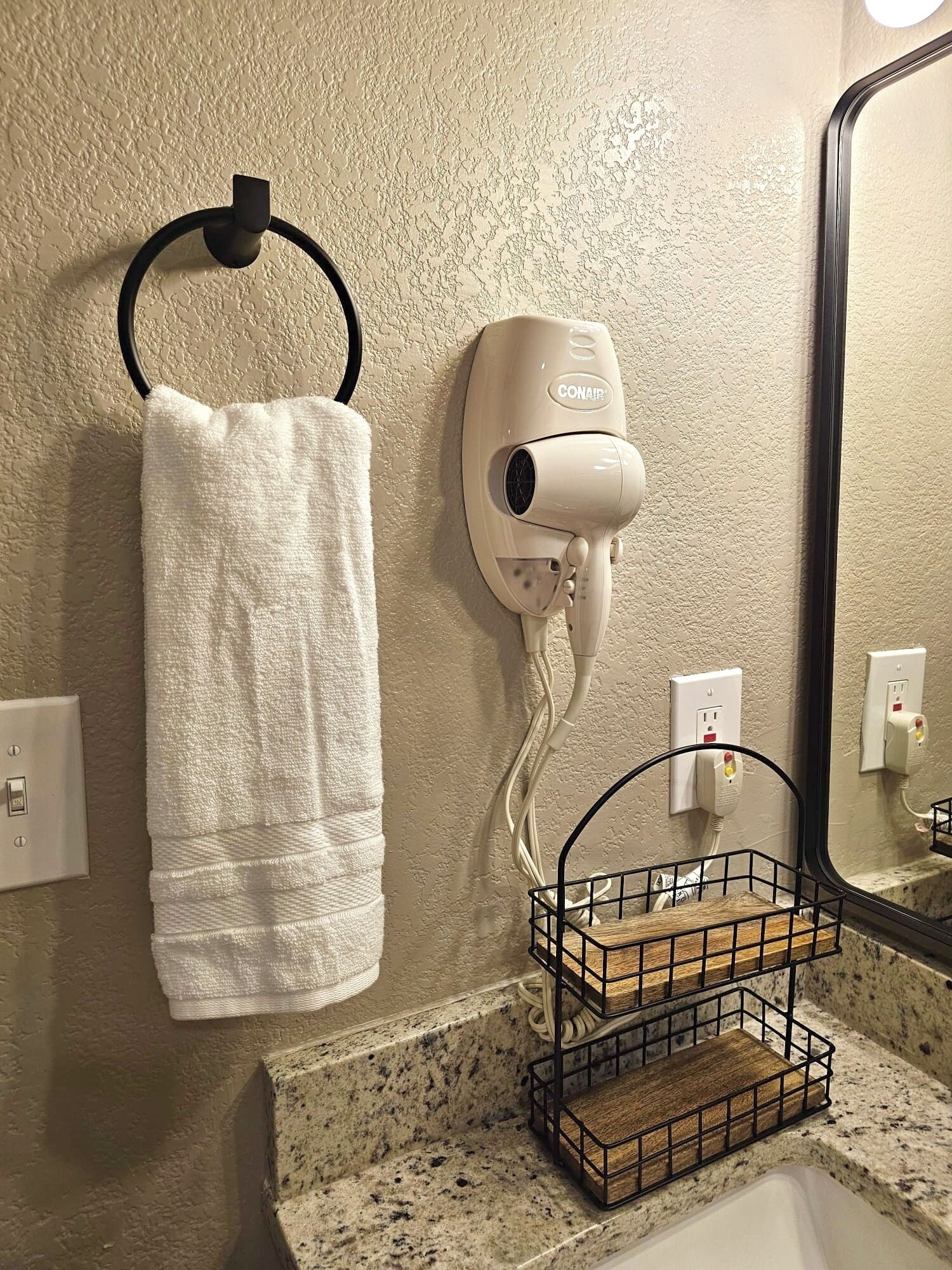 A bathroom with a towel rack, a hair dryer, a mirror, and a wooden shelf.
