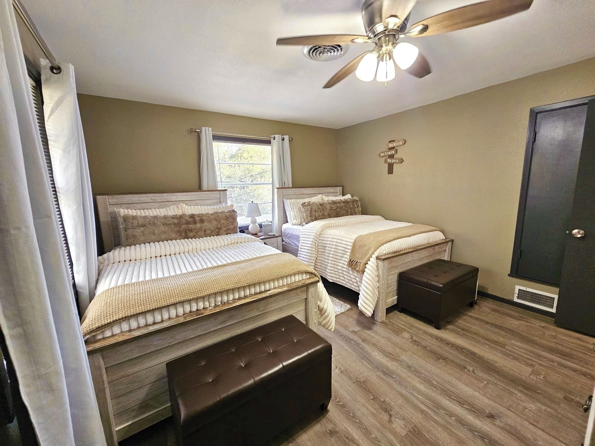 A bedroom with two beds, a ceiling fan, a window with curtains, and a door.