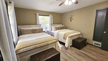 A bedroom with two beds, a ceiling fan, a window with curtains, and a door.