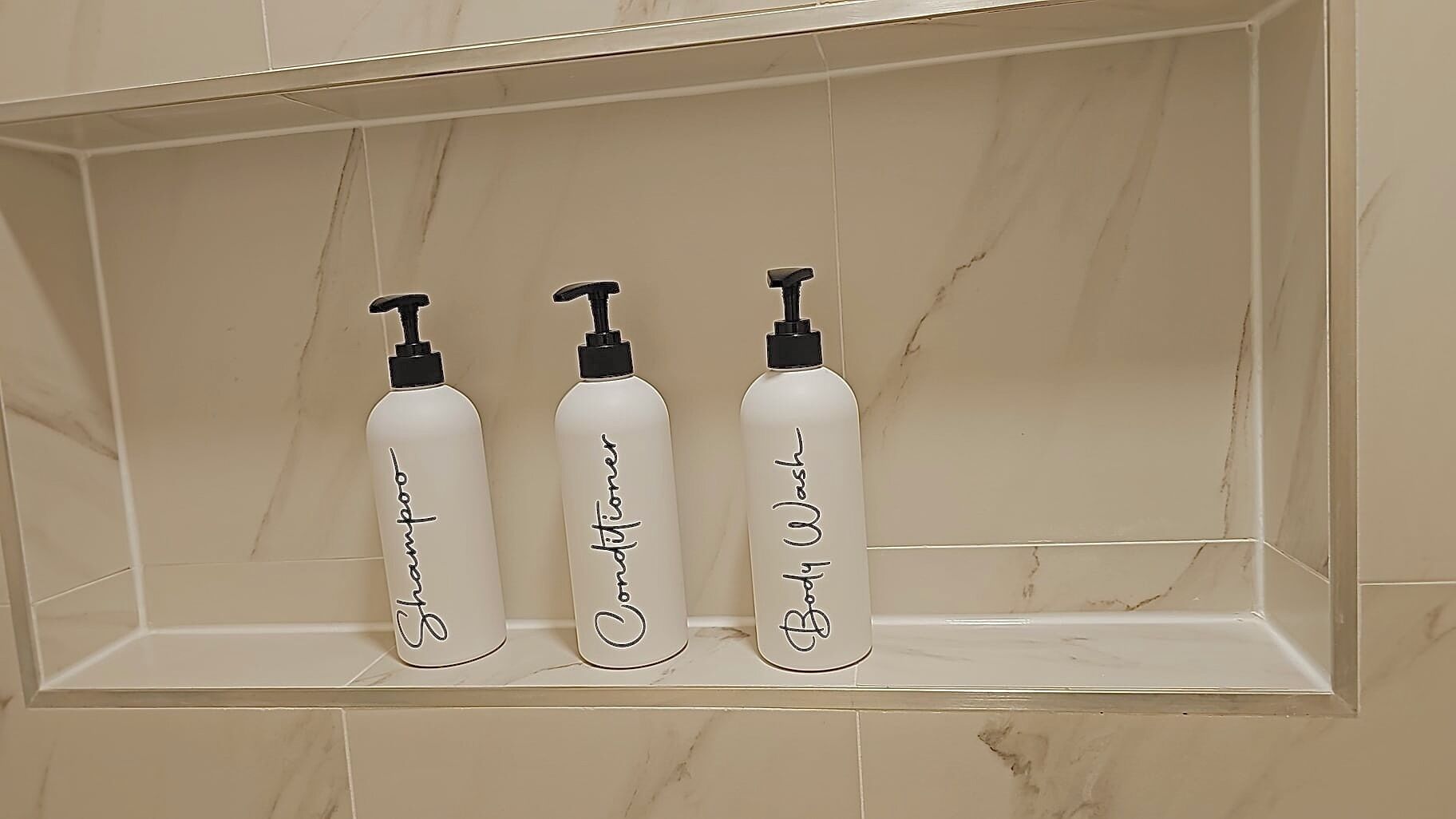 Three white bottles with black pumps on a beige tiled shelf.
