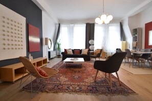 A modern living room with a sofa, coffee table, and chairs. There is a large rug, a wooden cabinet, and a wall with a decorative panel.