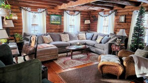 A cozy log cabin interior with a sectional sofa, a small dining table, wicker chairs, and a Christmas tree. - Lovely Log Cabin Retreat: Cozy Fireplace, Beautiful Gardens & Nature (Bradford)