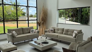 A modern living room with a sectional sofa, a coffee table, and a large window offering a view of greenery. - Complete House in Porto Sauipe (Subaúma)