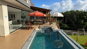 A modern hotel with a swimming pool, outdoor seating, and a covered patio area. - Complete House in Porto Sauipe (Subaúma)